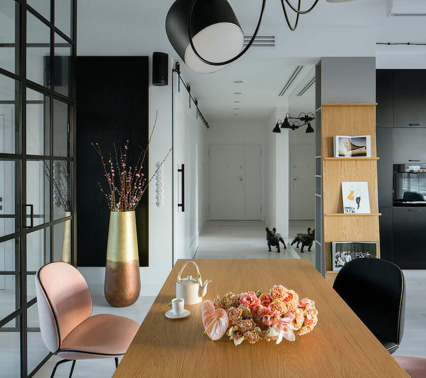 Jadalnia z dużym drewnianym stołem przeszkloną ścianą z czarnymi szprosami i widokiem na czarną kuchnię w nowoczesnym mieszkaniu