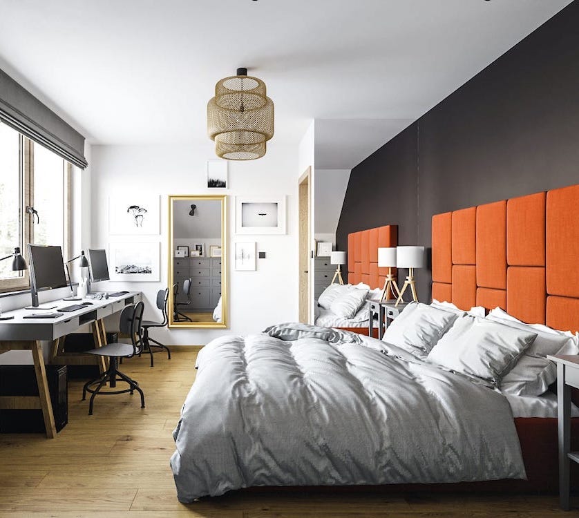 Przytulna sypialnia w mieszkaniu z dużym łóżkiem z pomarańczowym wezgłowiem i dwoma biurkami do pracy