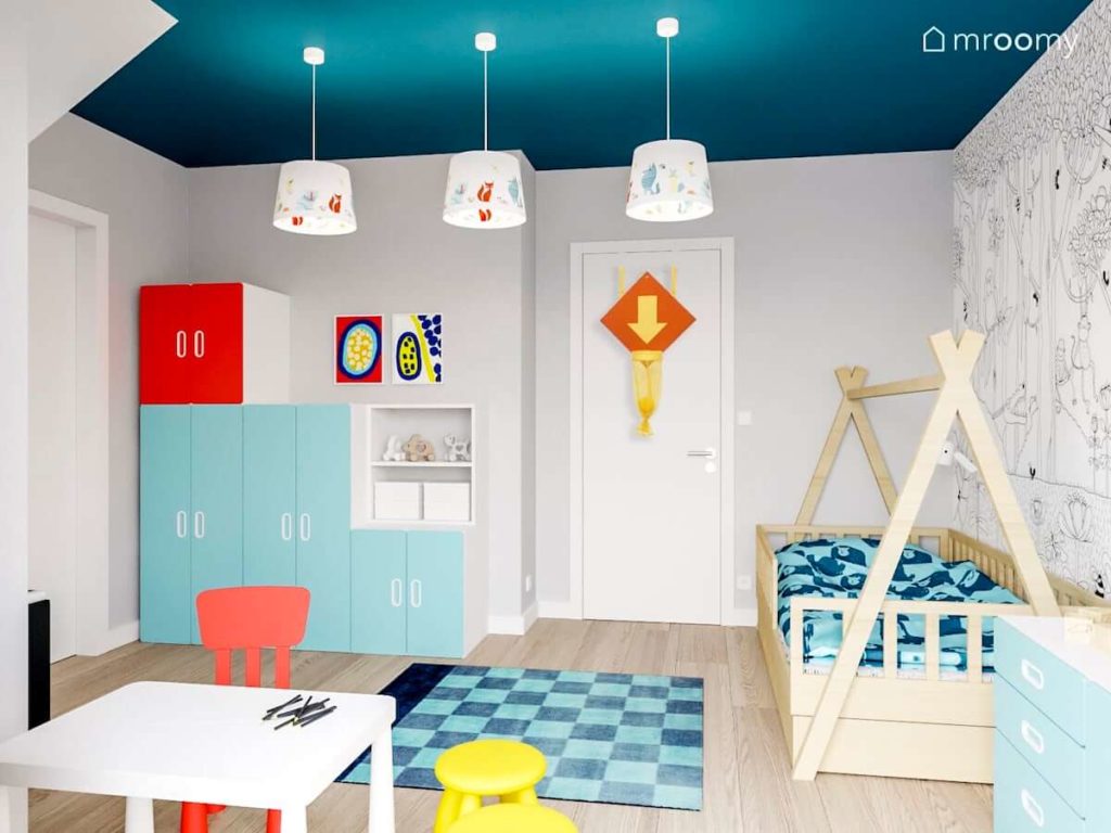 pokój chłopca na poddaszu z niebieskim sufitem dywan w niebieską kratkę łóżkiem tipi i białe lampami z kolorowymi zwierzątkami