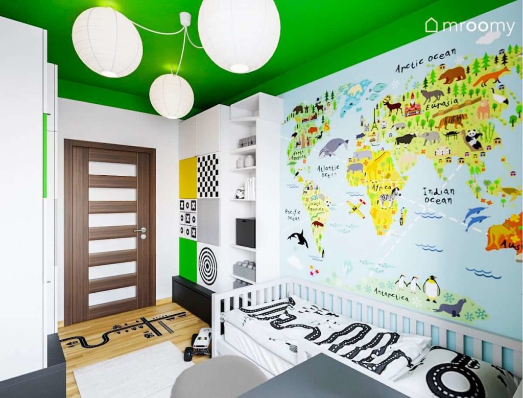 Tapeta z mapą świata przy łóżku w pokoju małego chłopca w którym jest kolorowy sufit i białe lampy