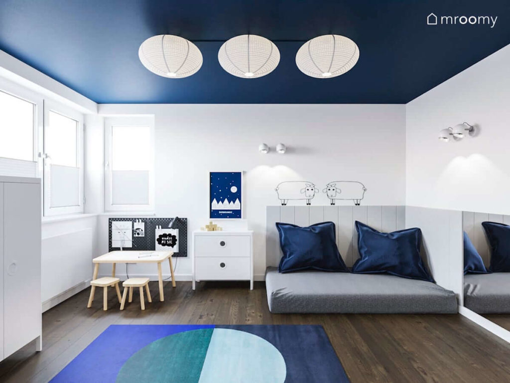 Miejsce do spania z miękkimi panelami ściennymi stoliczek z krzesełkami tapeta w owcami i niebieski dywan w minimalistycznym pokoju małego chłopca