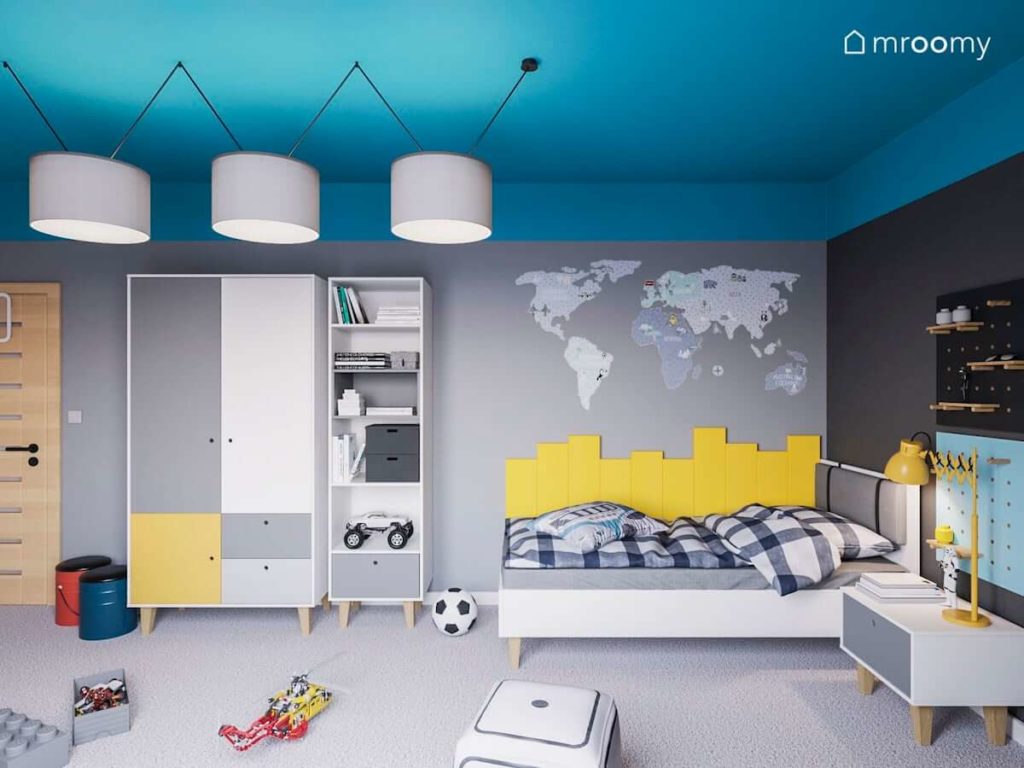 Pokój dziecka z niebieskim sufitem szarymi ścianami i naklejką mapą świata nad białym łóżkiem obok regału młodzieżowego