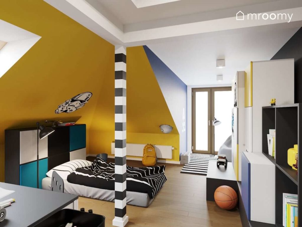 Skosy pomalowane na żółto obok łóżka w formie materaca i zagłówka z mebli z naklejonymi miękkimi panelami ściennymi w pokoju nastoletniego chłopca.