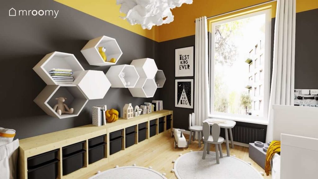 Czarna ściana z heksagonalnymi półkami szary stoliczek z krzesełkami i żółty sufit w pokoju dwóch małych chłopców