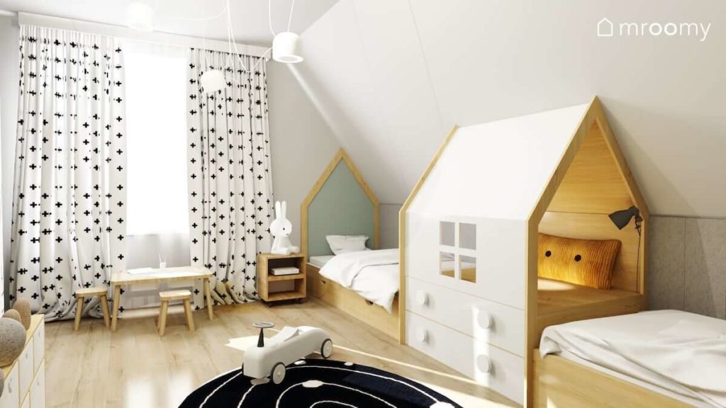 Łóżka z zagłówkami w kształcie domków i kryjówką na środku zasłony w krzyżyki i dywan z motywem w kosmosu w pokoju dwóch przedszkolaków.