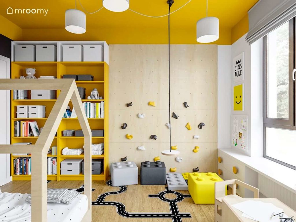 Huśtawka i ścianka wspinaczkowa obok żółtych regałów w pokoju małej dziewczynki