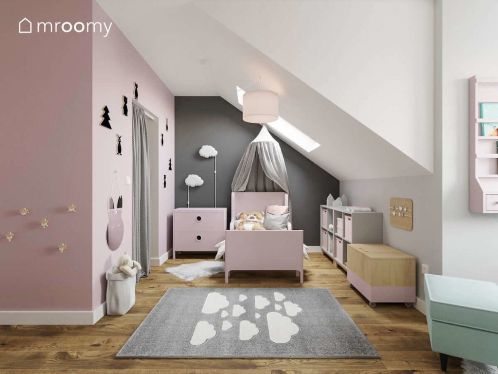 Różowe łóżko z baldachimem i z komodą na tle szarej ściany obok różowej garderoby w pokoju dziewczynki.