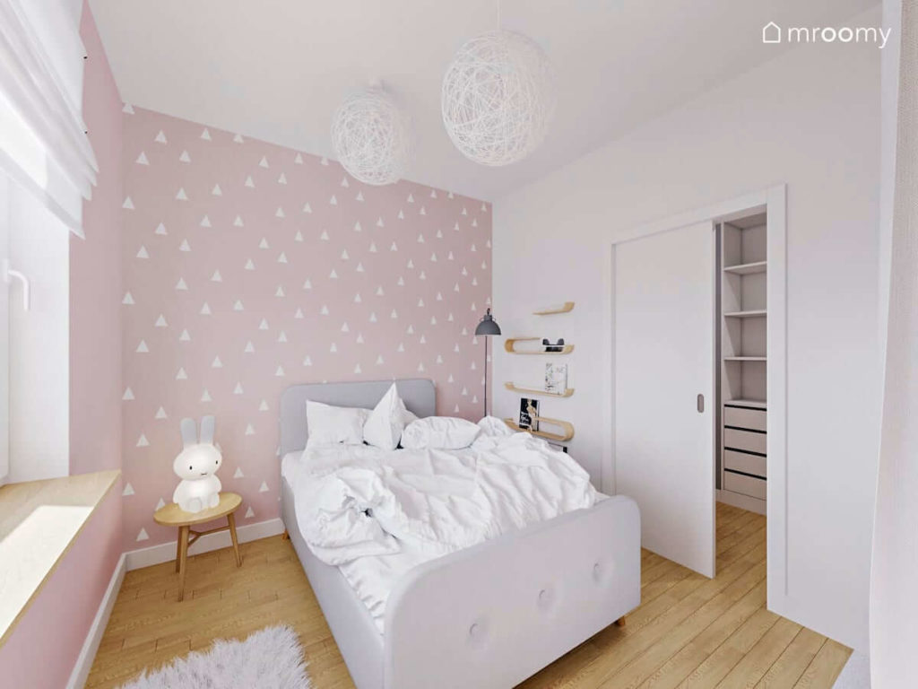 Sypialnia dziewczynki z dużym tapicerowanym łóżkiem i różową tapetą w białe kropki