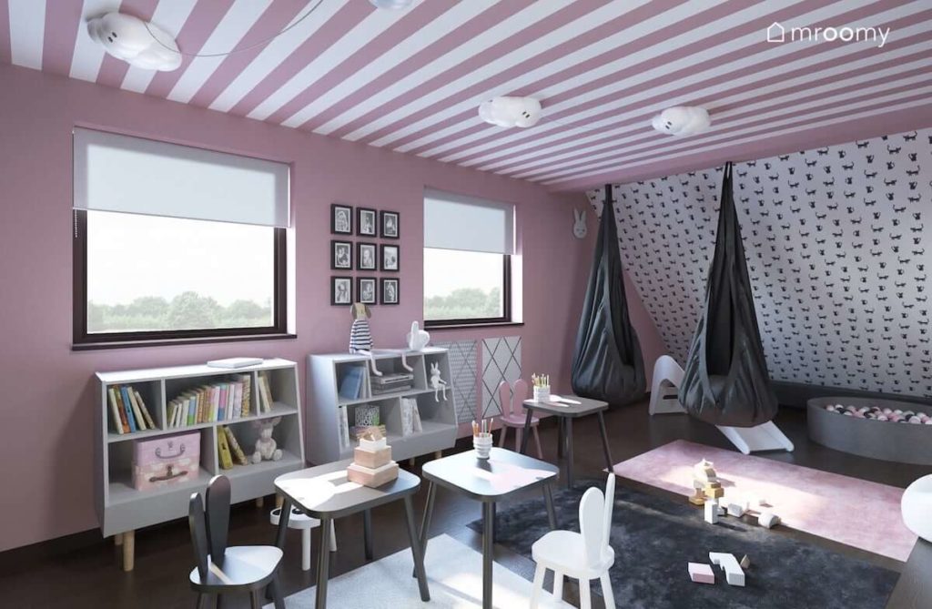 Miejsce do zabawy ze stoliczkami i krzesełkami w królicze uszy w poddaszowym pokoju dla dwóch małych dziewczynek z różowymi pasami na suficie i różowymi ścianami