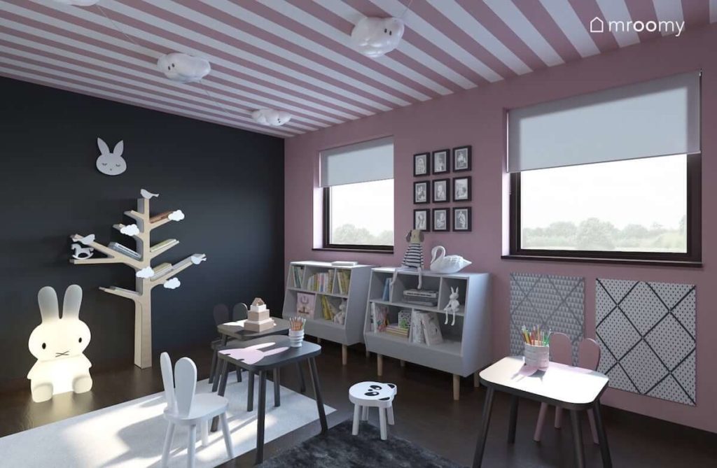 Regał-drzewko półki na książki drewniane dziecięce krzesełka i stoliczek w pokoju dla małych dziewczynek z szarą ścianą i różową tapetą