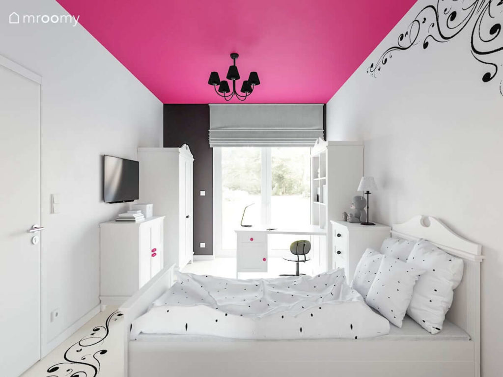 Białe meble w pokoju dziewczynki z różowym sufitem i czarną naklejką w kwiaty na ścianie i podłodze