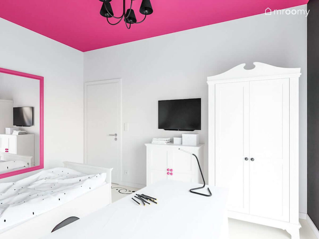 Biała komoda i szafa w pokoju dziewczynki z czarną lampą i różowym sufitem