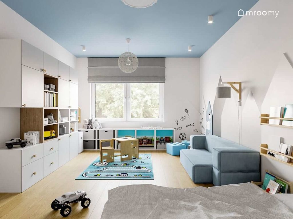 Pokój małego chłopca z niebieskim sufitem stoliczkiem z krzesełkami białą szafą i niebieską sofą