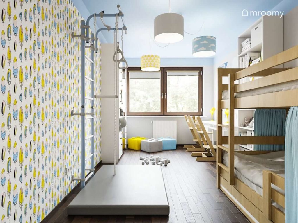 Drabinka i materac przy ścianie z tapetą w pióra miękkie pufy w kształcie klocków lego w pokoju dwóch dziewczynek lub chłopców z piętrowym drewnianym łóżkiem
