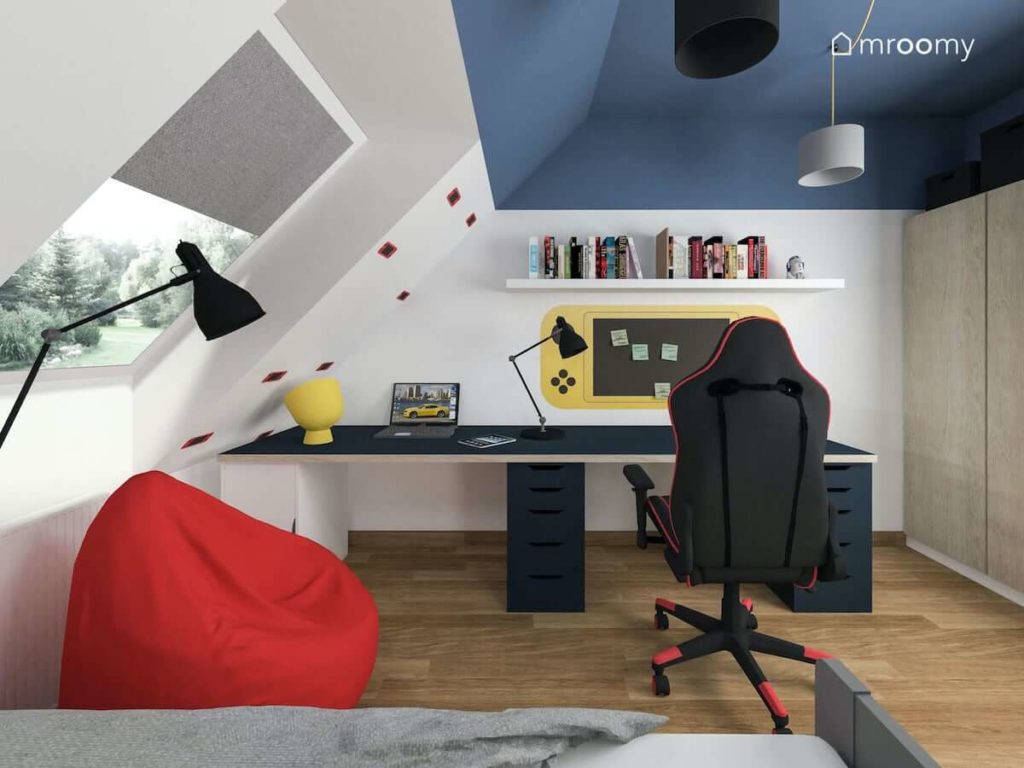 Duże biurko dla nastolatka grającego w gry komputerowe z gamingowym fotelem obok którego jest czerwony worek sako