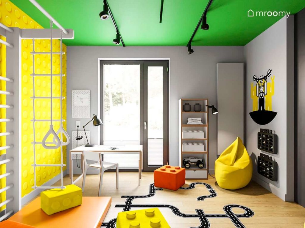 Pokój chłopca z biurkiem i krzesłem ze sklejki zielonym sufitem i żółtą tapetą w klocki lego