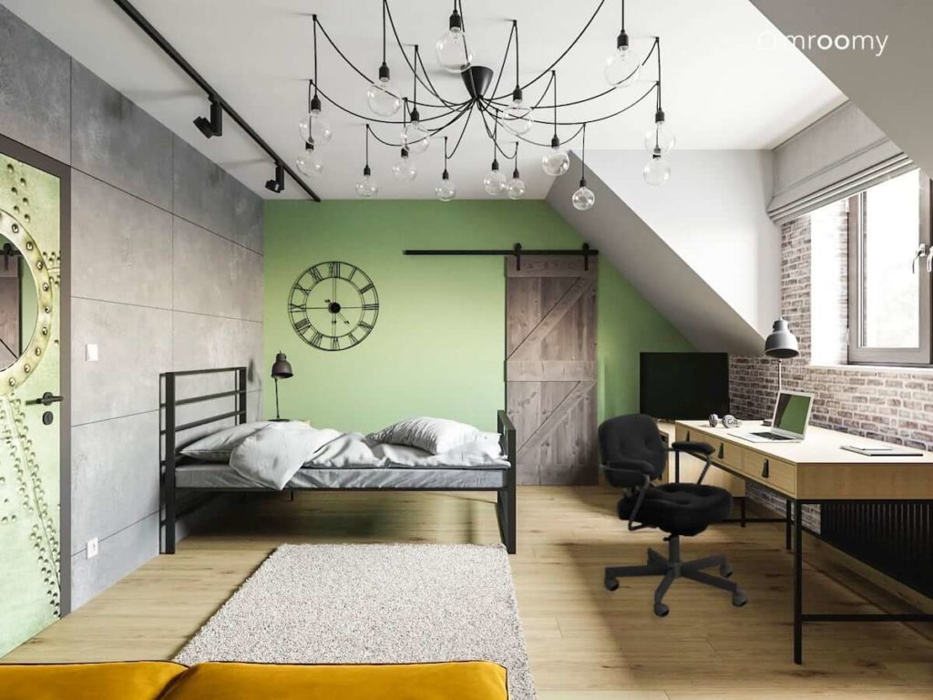 Metalowe łóżko zielona ściana z drzwiami do garderoby drewniane biurko i dywan w loftowym pokoju nastolatka