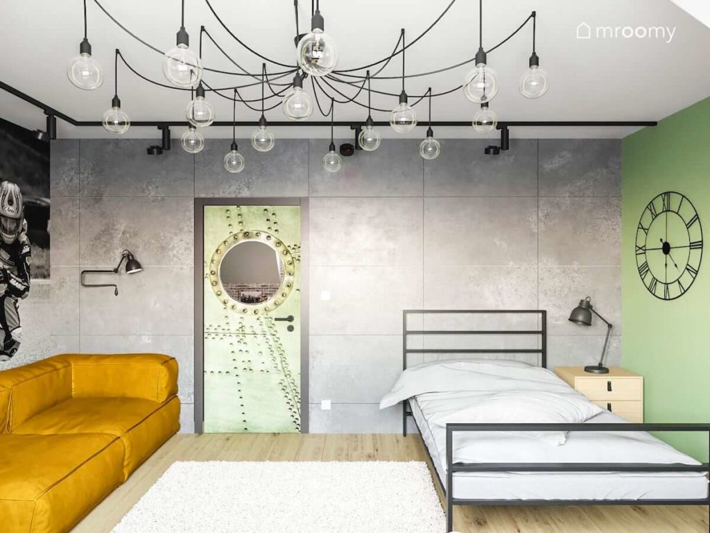 Betonowe ściany w pokoju nastolatka gdzie znajduje się żółta miękka sofa i metalowe łóżko