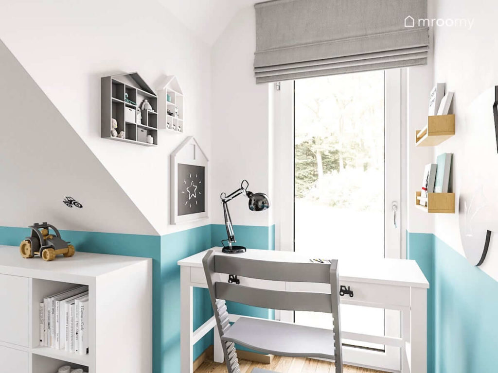 Białe biurko przy oknie z szarą roletą rzymską i turkusowym kolorem na ścianie w pokoju dla chłopca