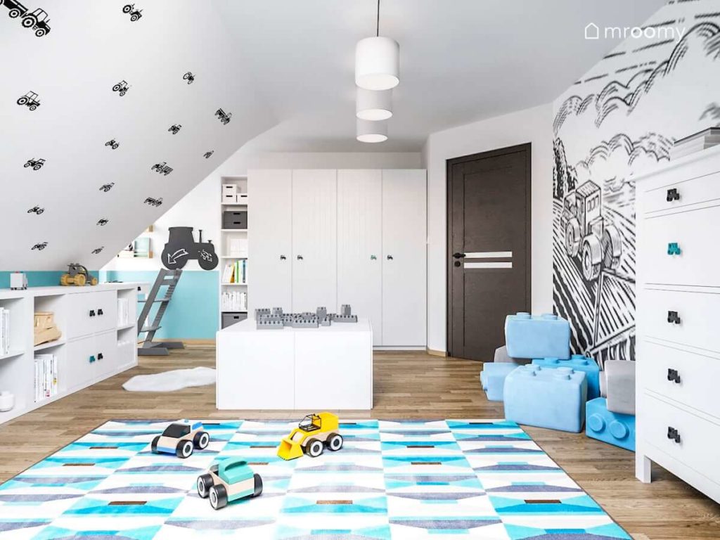 Niebieski dywan we wzorki i ściany w naklejki traktorki w pokoju małego chłopca z białymi meblami