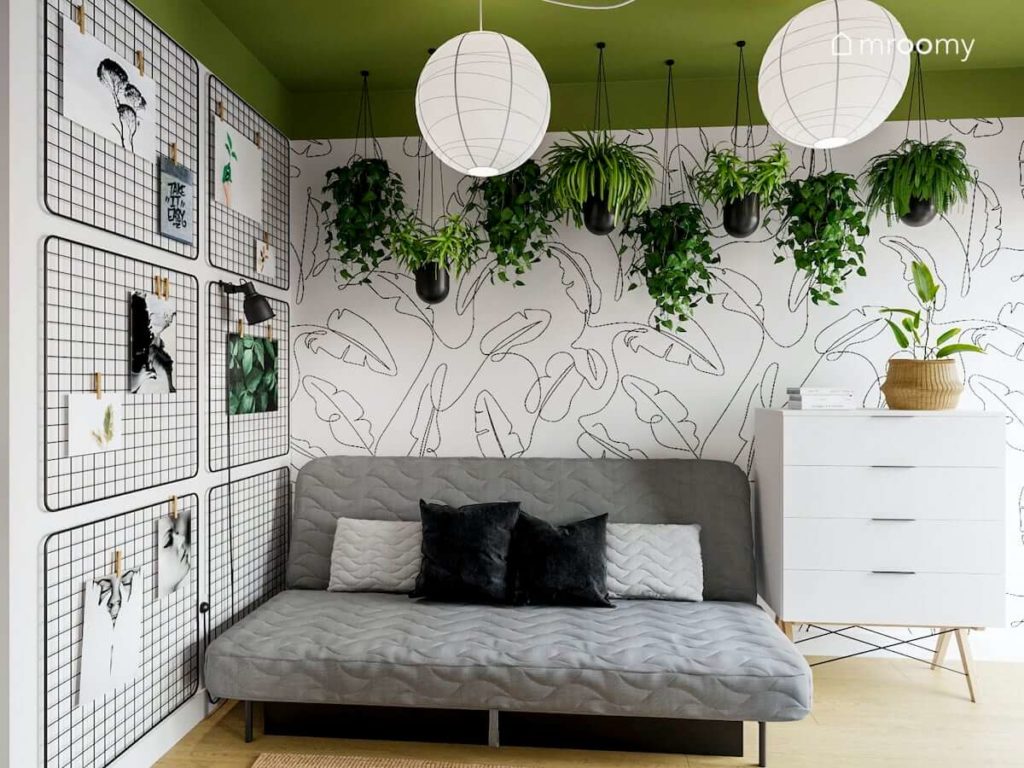 Rozkładana sofa organizery na ścianie tapeta w motywy kwiatów i kwiaty zwisające z sufitu w pokoju nastolatki