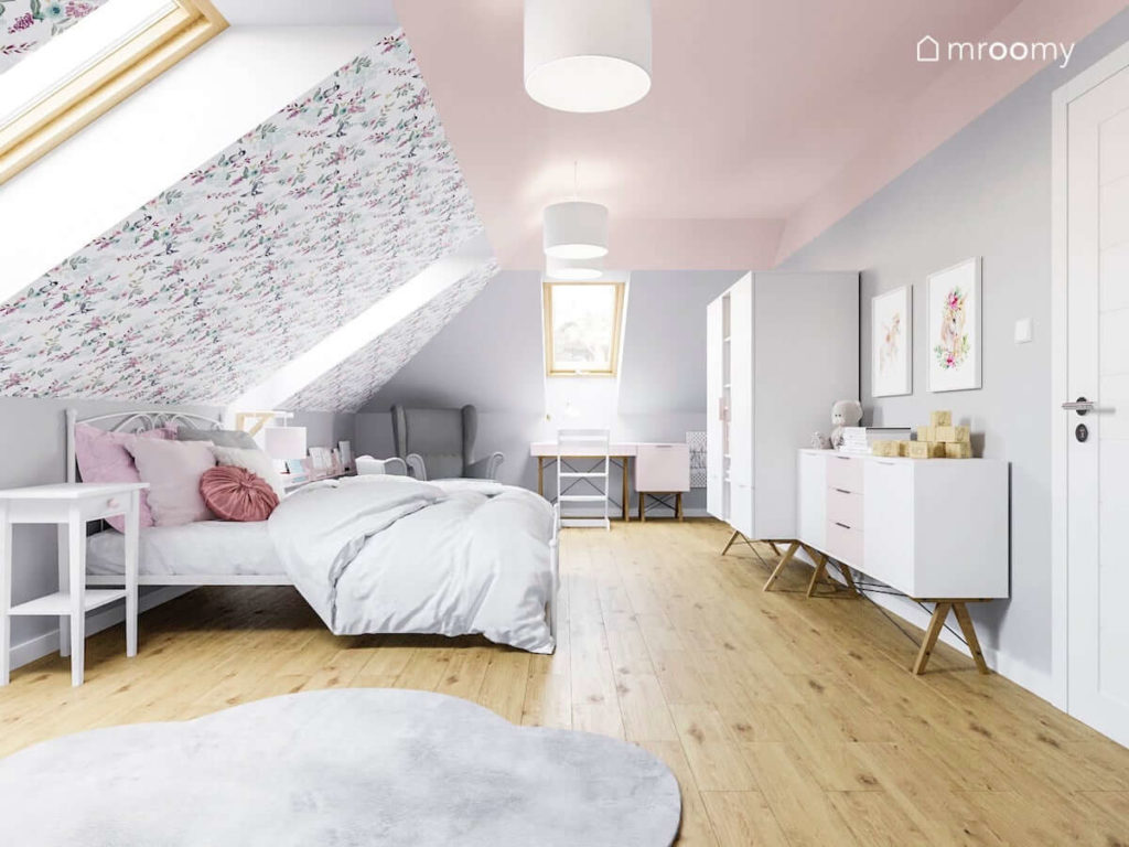 Pokój dziewczynki na poddaszu z dużym łóżkiem białymi meblami różowym sufitem szarymi ścianami i tapetą w kwiaty