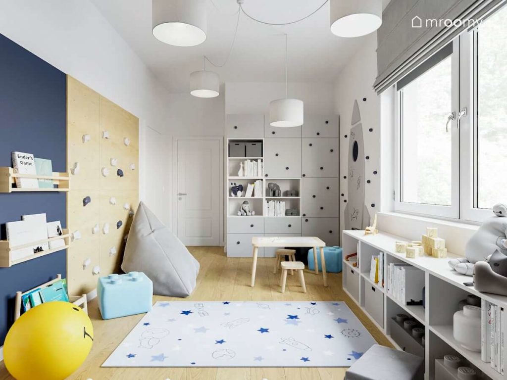 Pokój małego chłopca ze stoliczkiem ścianką wspinaczkową workiem sako szafą pufami lego i dywanem w gwiazdy