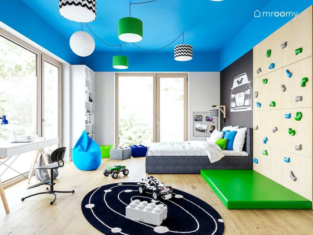 Pokój chłopca w niebieskie zielone czarne białe kolory ze ścianką wspinaczkową dużym łóżkiem i kolorowym sufitem