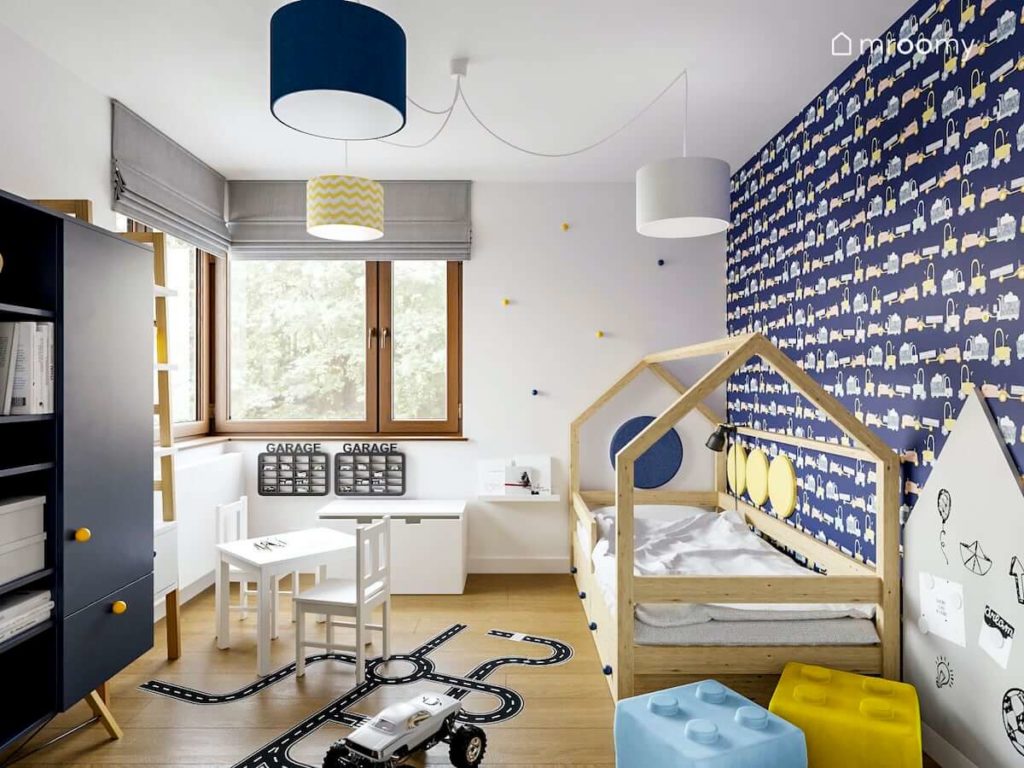Granatowa tapeta w pojazdy łóżko domek biały stolik i naklejki podłogowe jezdnie w pokoju małego chłopca