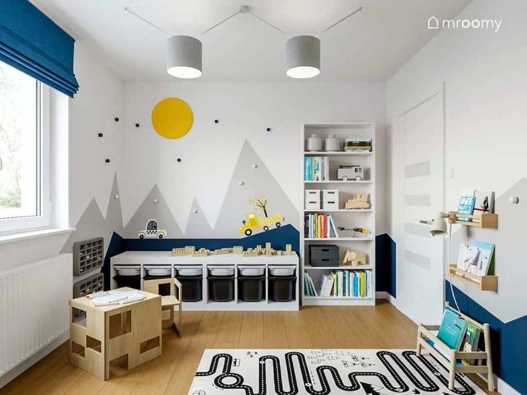 Pokój małego chłopca z motywem gór na ścianie i jasnymi meblami z szarym dywanem droga