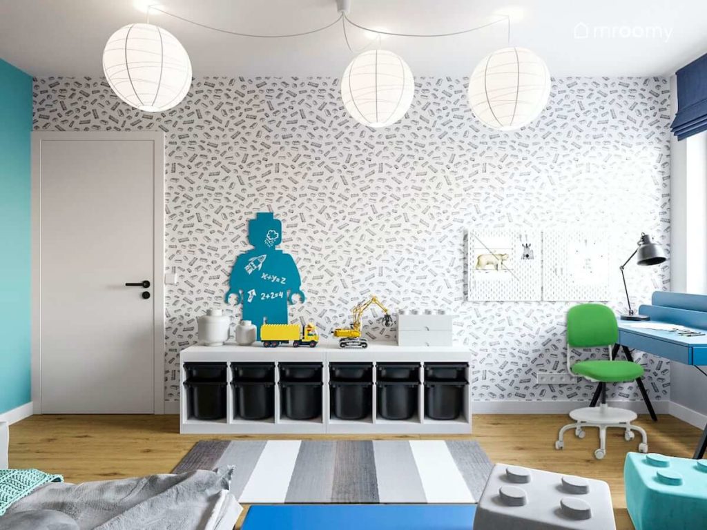 Ściana z tapetą z motywem lego białe abażury dywan w paski i zielone krzesło do biurka w pokoju szkolnego chłopca