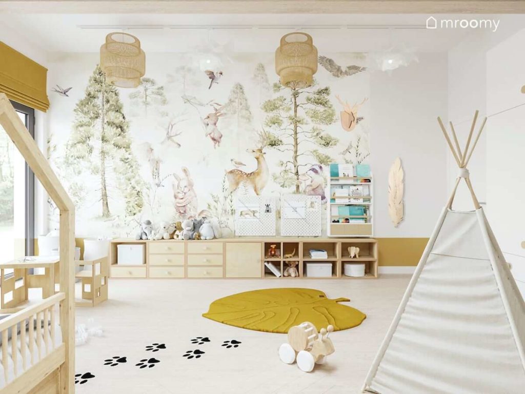 Leśna tapeta w pokoju małego chłopca z dywanem meblami ze sklejki i jasnymi tipi obok naklejki podłogowe