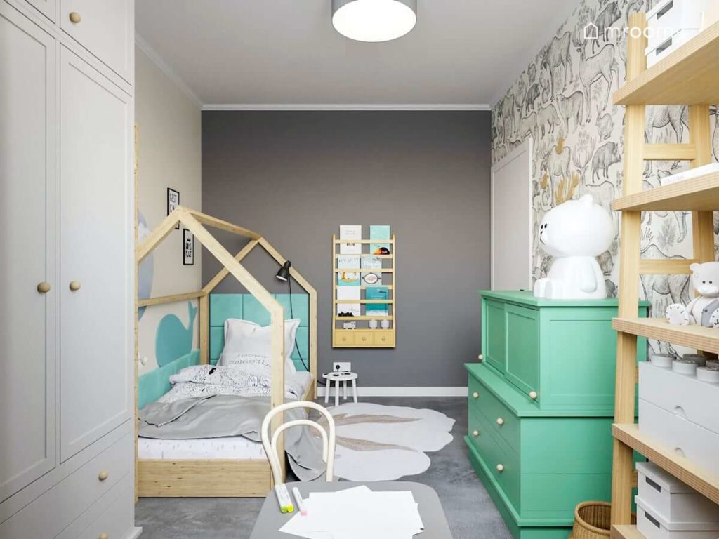 Leśny pokój małego chłopca z łóżkiem domkiem i zieloną komodą na której stoi lampka miś