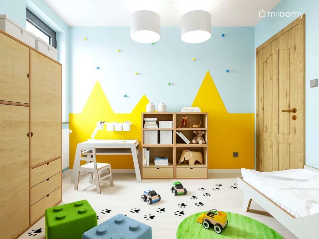 Pokój małego chłopca z meblami ze sklejki i tapetą w żółte góry ze śladami łapek na podłodze