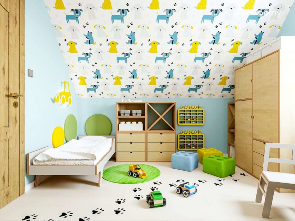 Łóżko z białej sklejki obok miękkie panele ścienne niebieskie ściany tapeta ze zwierzątkami i sklejkowe meble w pokoju przedszkolaka