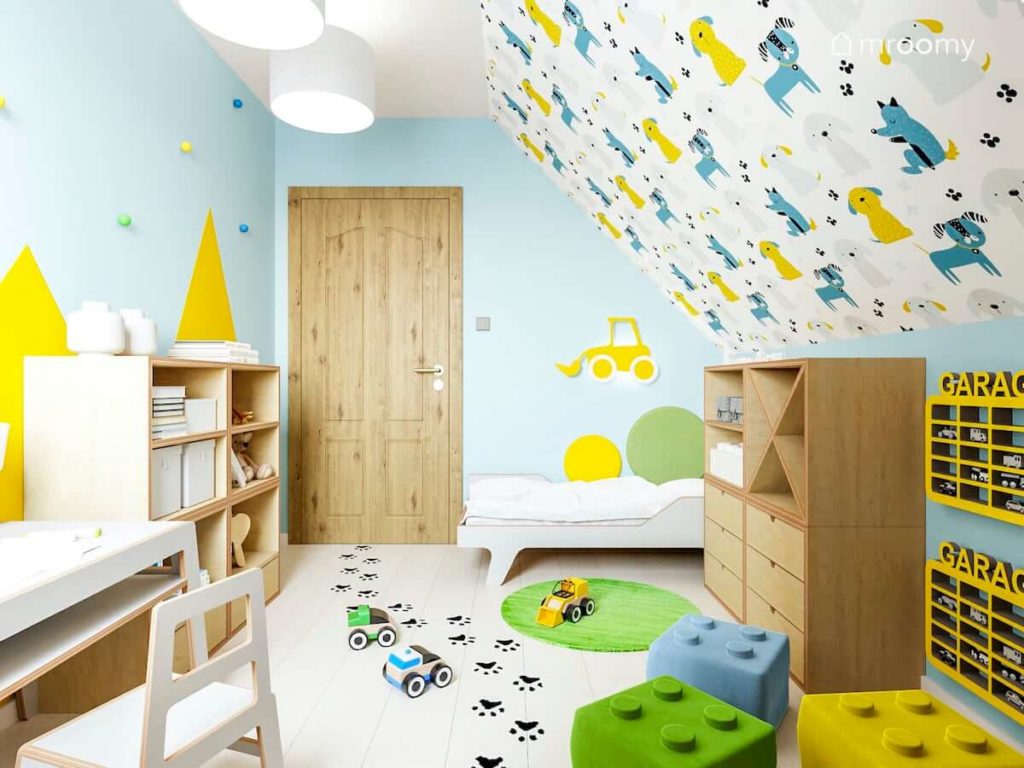 Jasno niebieskie ściany i tapeta w zwierzątka w pokoju małego chłopca z jasnymi meblami