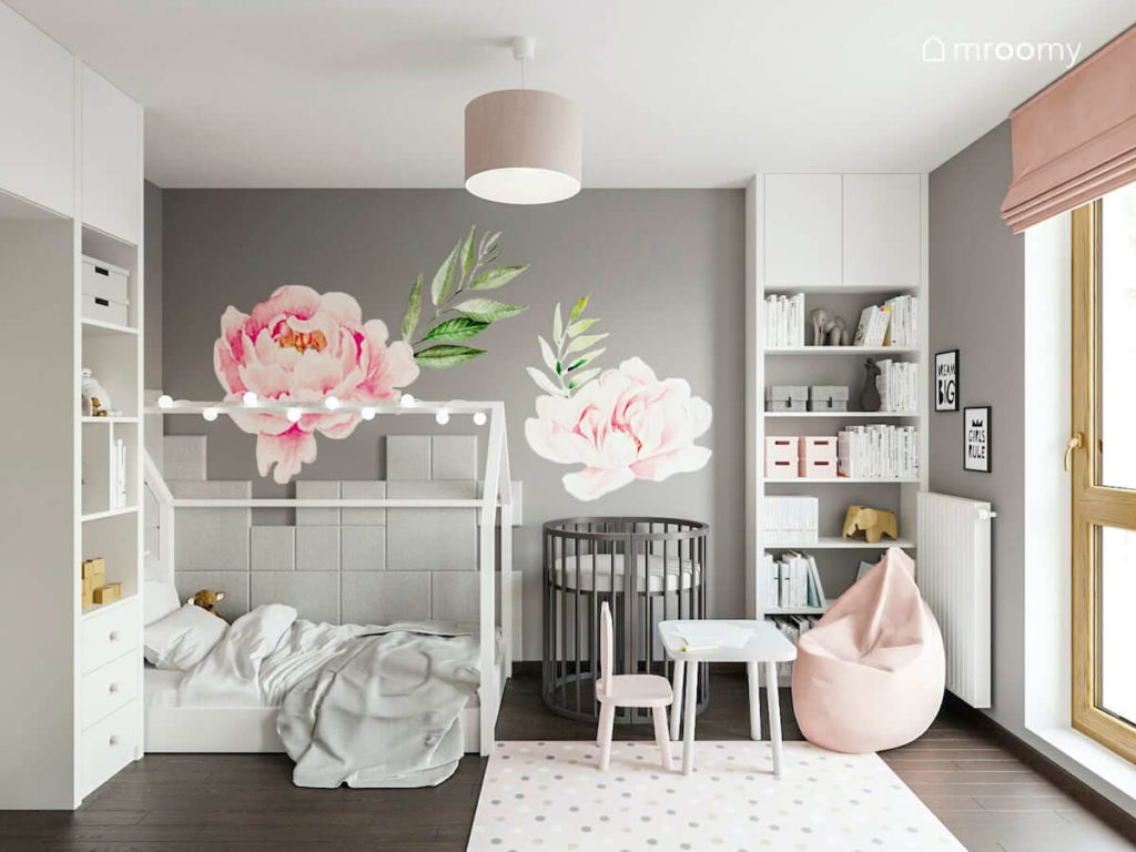 Łóżko domek i drugie rosnące z dzieckiem łóżko dla niemowlaka w pokoju dwóch dziewczynek z szarymi ścianami i naklejkami piwoniami
