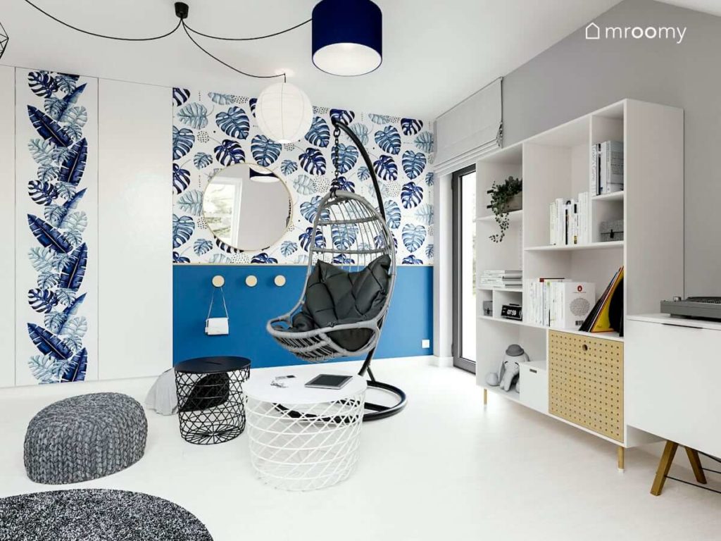 fotel na tle niebieskiej ściany z motywem roślinnym biała podłoga i wiele abażurów w lampie w pokoju nastolatki