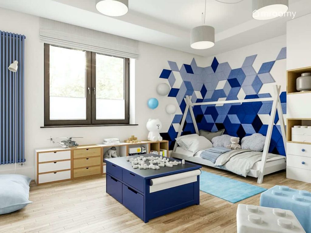 Łóżko tipi niebieskie panele ścienne niebieski stolik do zabawy klockami i regały pod oknem ze sklejki w pokoju małego chłopca