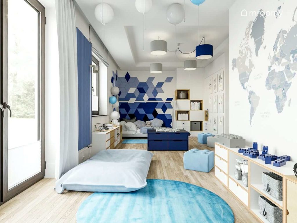 Pokój chłopca przedszkolaka ucznia z łóżkiem tipi niebieskimi miękkimi panelami ściennymi szarymi abażurami lampami balonami tapetą z mapą świata i pufami lego