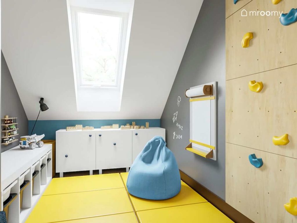 Strefa zabawy w pokoju chłopca z żółtymi materacami niebieskim workiem sako ścianką wspinaczkową i białymi niskimi komodami