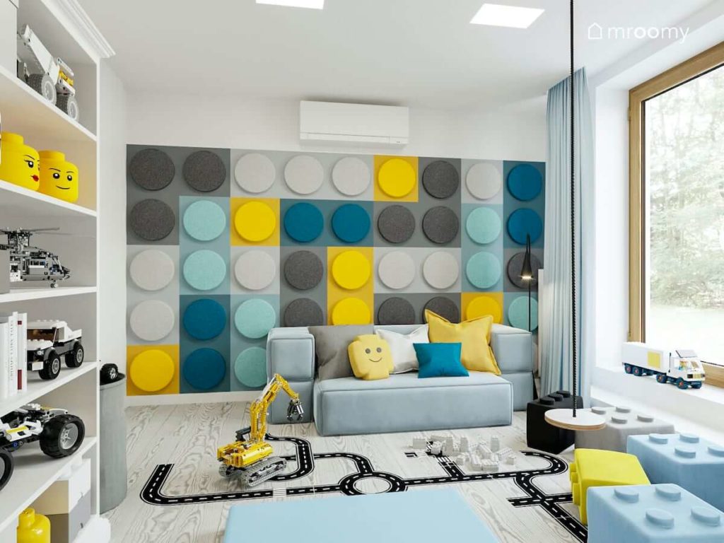 Ściana z miękkich paneli w kształcie klocków lego niebieska sofa naklejki podłogowe i huśtawka w pokoju bawialni dwóch chłopców