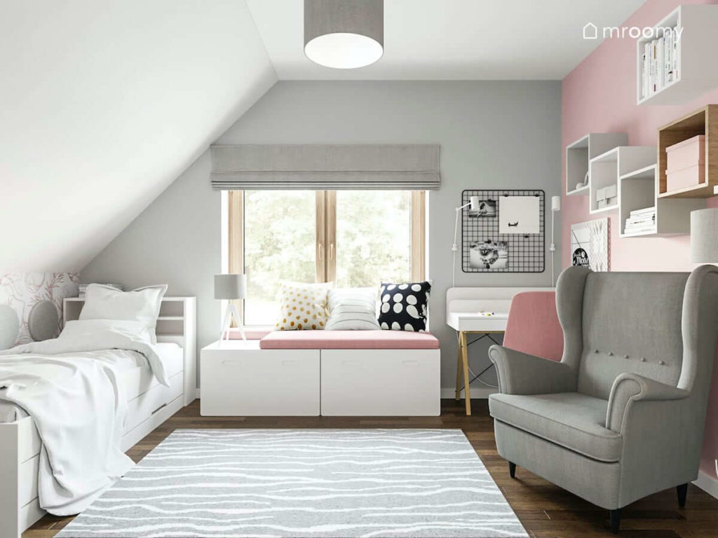 Siedzisko pod oknem białe łóżko szary fotel ściany białe szare i różowe w pokoju szkolnej dziewczynki