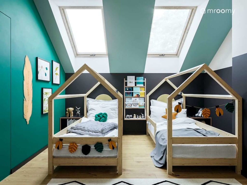 Łóżka domki z naturalnego drewna pod skosem z oknami w pokoju dwóch małych chłopców na tle czarne ściany kolankowej obok zielonych ścian