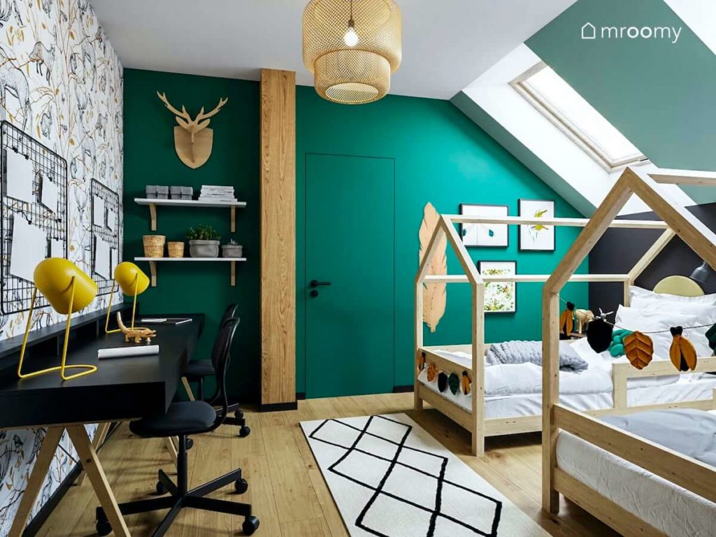 Pokój dla bliźniaków na poddaszu z łóżkami domkami czarnymi biurkami zielonymi ścianami i tapetą we wzory
