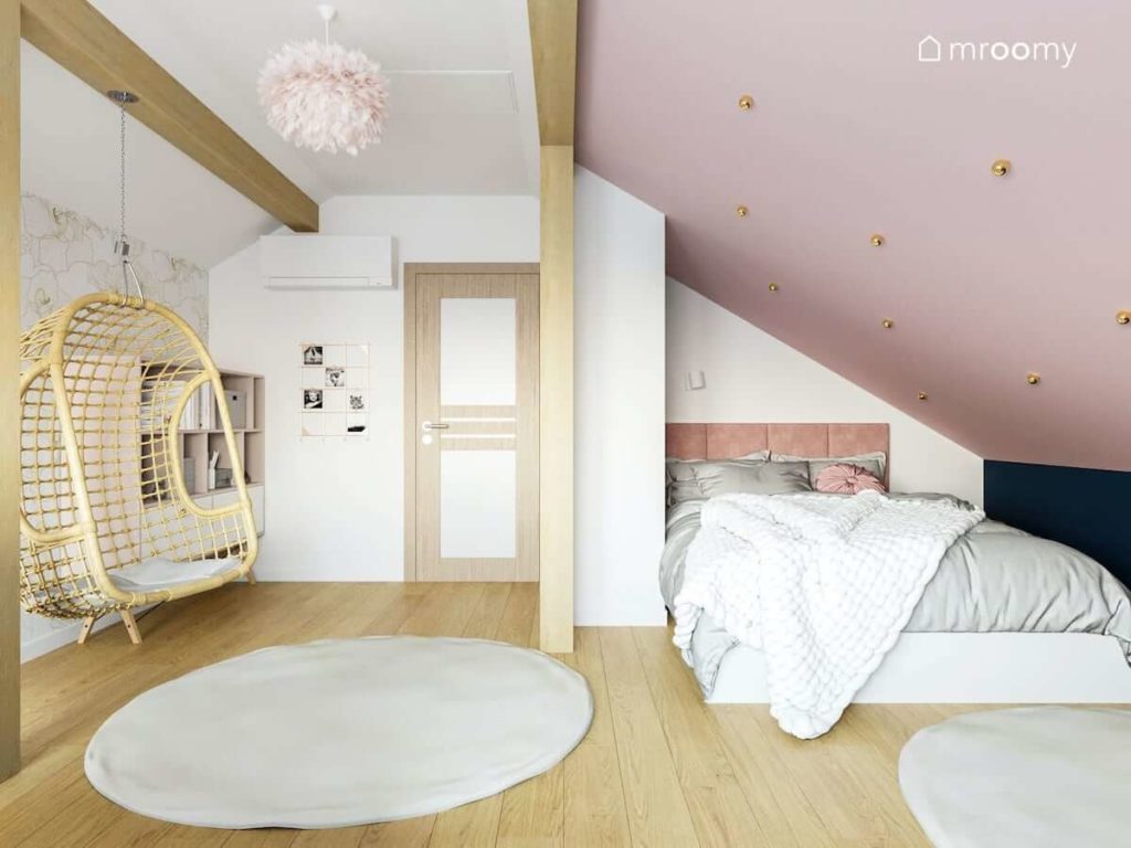 Duże łóżko do spania pod skosem w pokoju nastolatki z różowym sufitem szarym dywanem i belkami z drewna