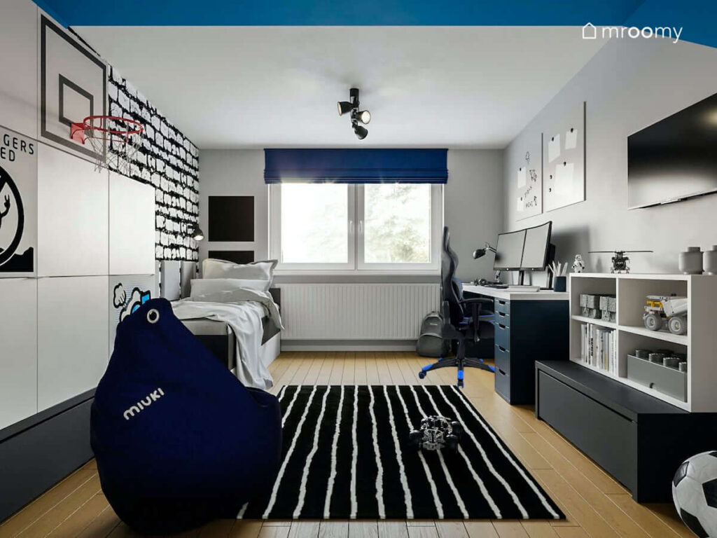 Pokój nastolatka z biało niebieskimi ścianami oraz meblami i dodatkami w podobnych kolorach na podłodze dywan w paski oraz pufa sako