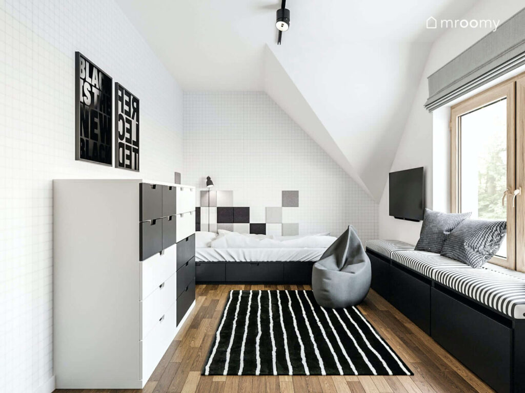 Czarno biały pokój dla nastolatka z łóżkiem z szufladami pojemną komodą i tapicerowanym siedziskiem oraz dywanem w paski i pufą sako