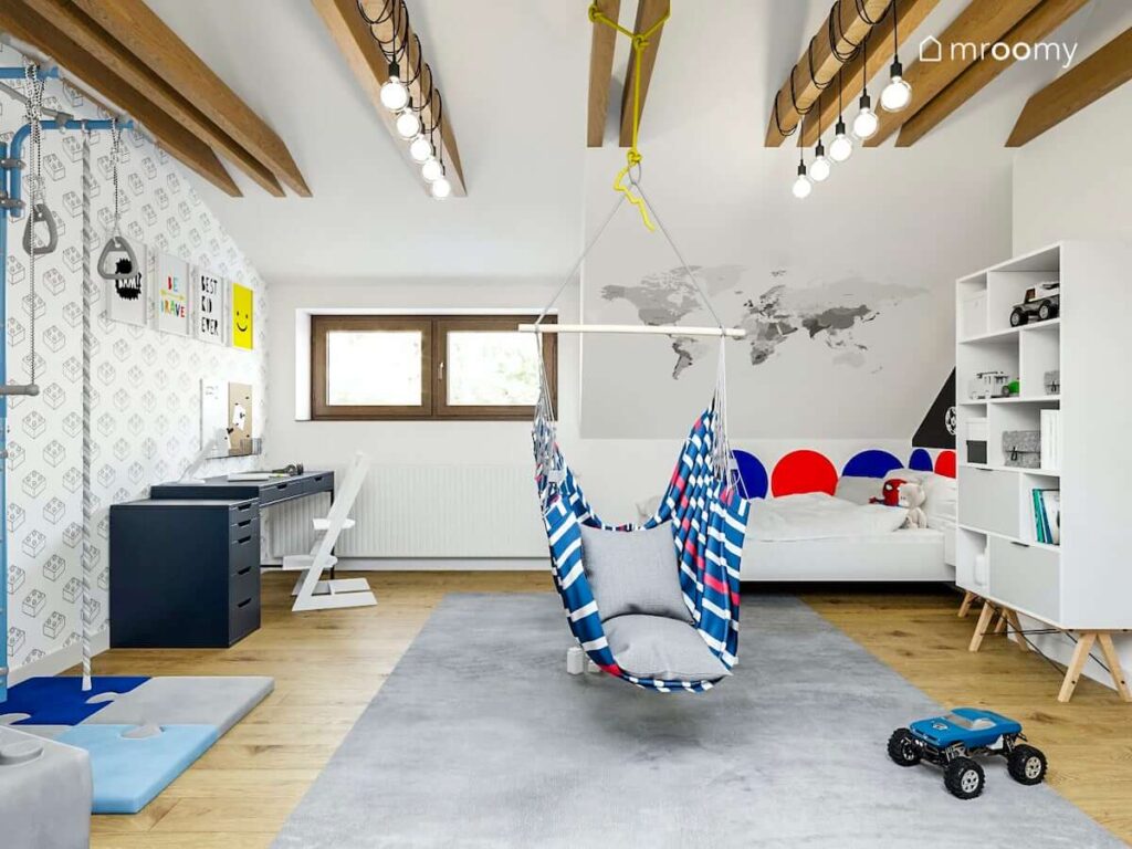 Jasny pokój z białymi ścianami łóżkiem ozdobionym kolorowymi panelami ściennymi niebieskim biurkiem i dużym dywanem w pokoju kilkuletniego chłopca
