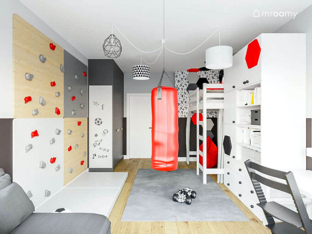 Czarno biało szary pokój dla chłopca z czerwonym workiem treningowym i pufą sako a także ścianką wspinaczkową dużym dywanem i materacem gimnastycznym